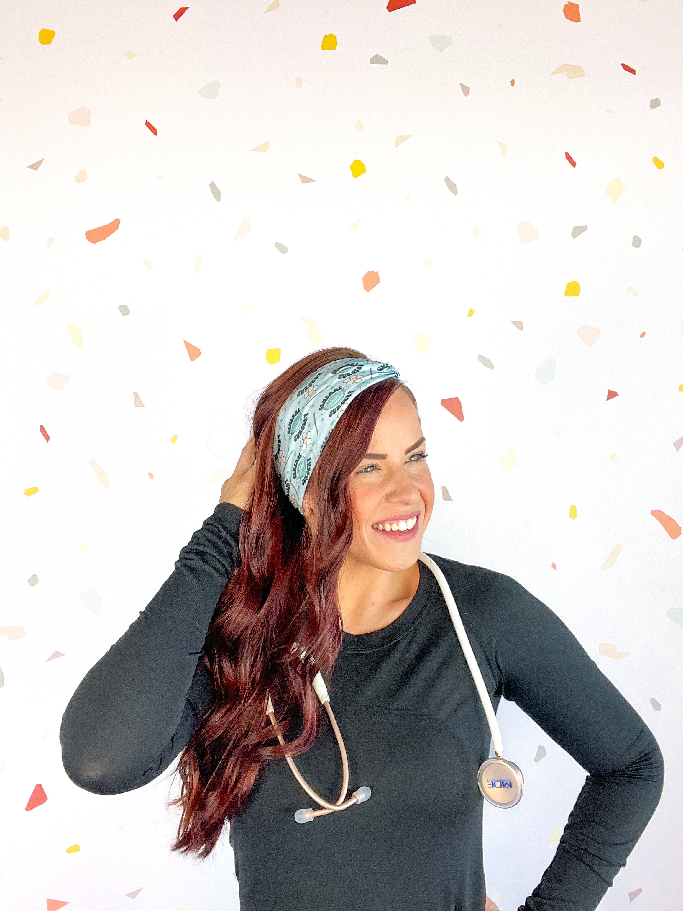 A woman confidently wears the Scrub In headband with a stethoscope, showcasing its versatile 3-in-1 twist style. Designed for function and style, perfect for workouts or workdays.