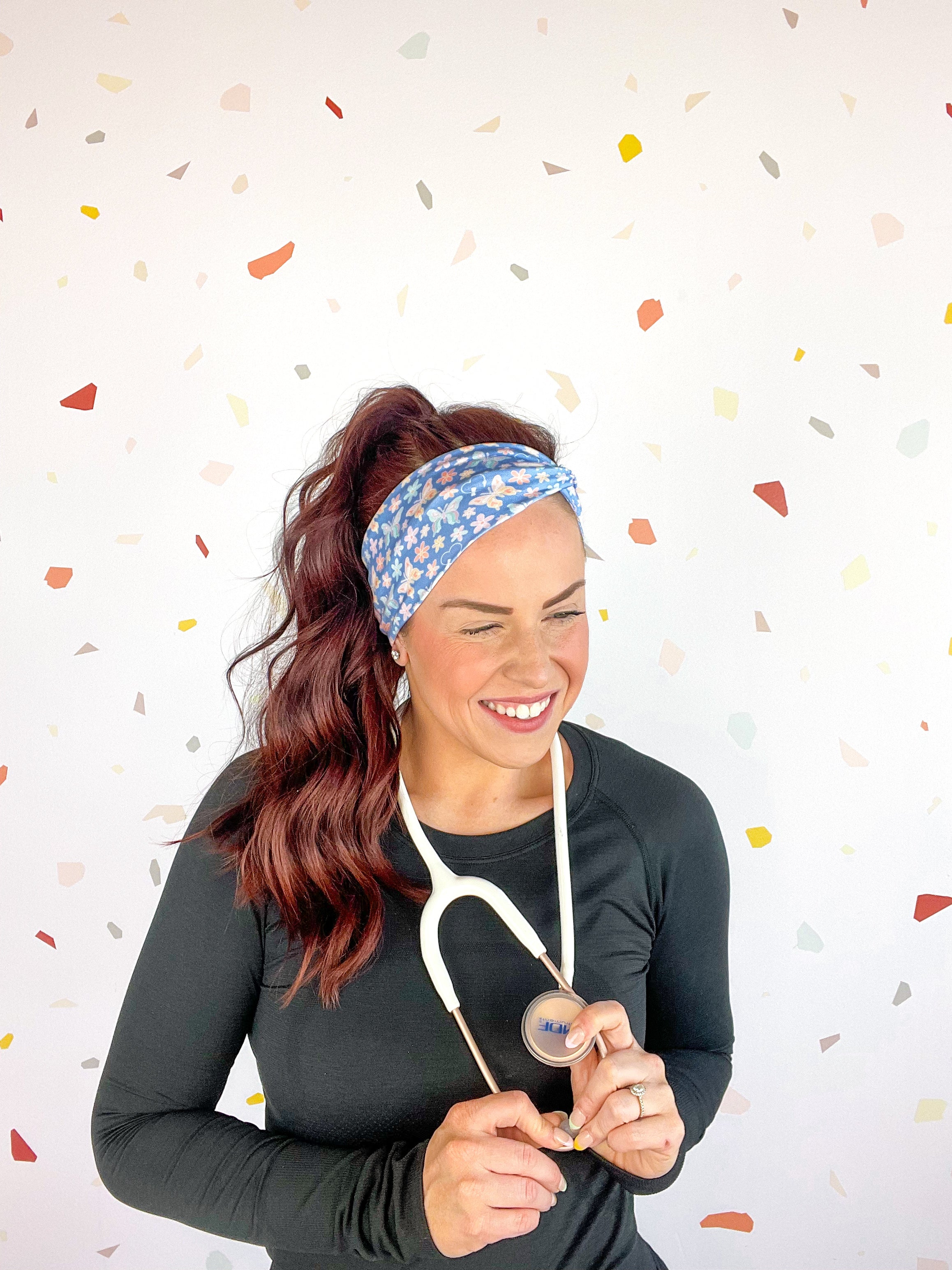 A woman confidently wears the Rainbows and Butterflies Headband, a functional twist-style accessory. Designed for comfort and versatility, machine washable with sweat-absorbent fabric. Perfect for workouts, shifts, or play.