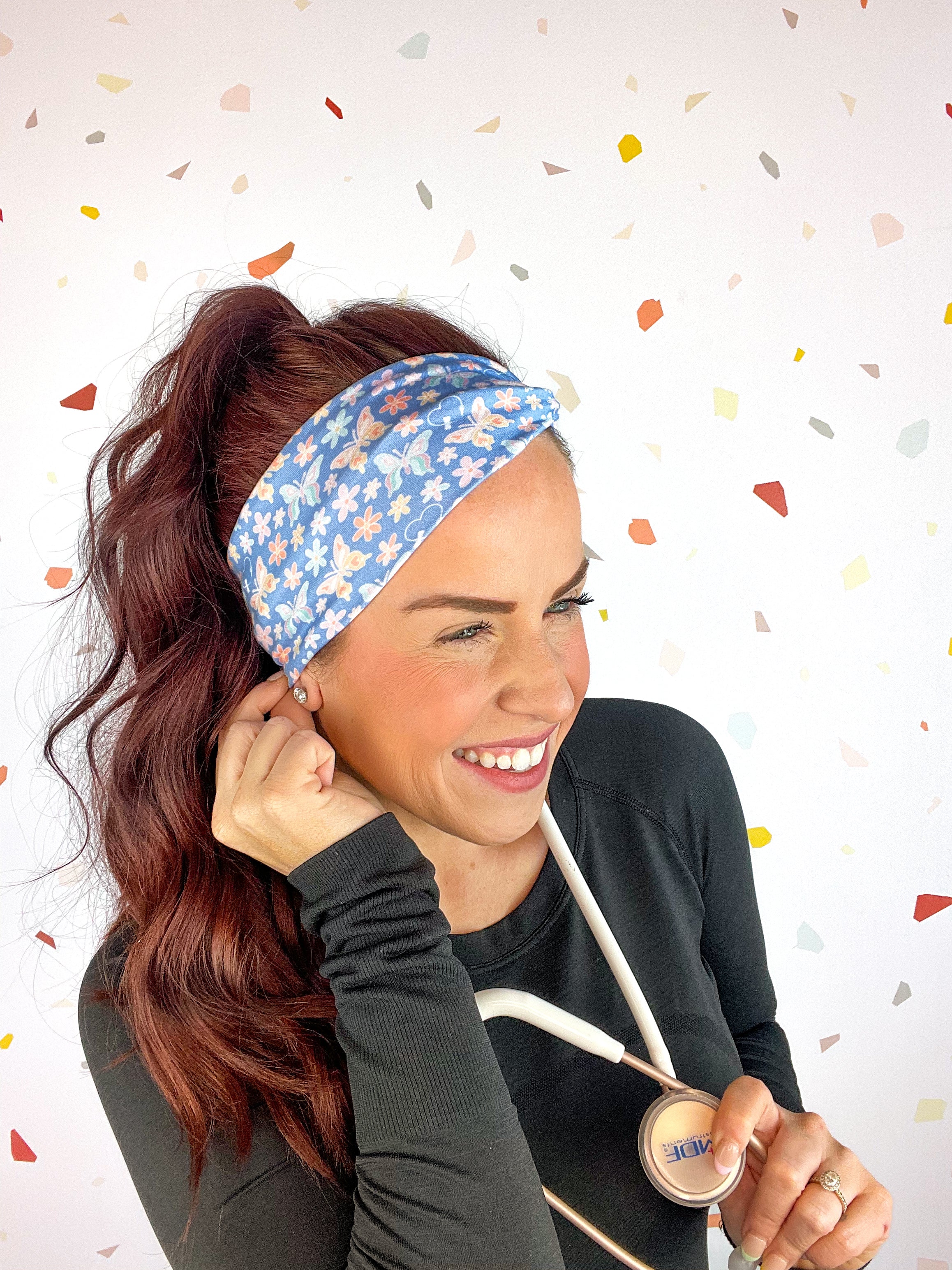 A woman confidently wears the Rainbows and Butterflies Headband, a functional twist-style accessory. Designed for comfort and versatility, machine washable with sweat-absorbent fabric. Perfect for workouts, shifts, or play.