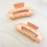 Checkmate Lilac Clip: a 3.6-inch glossy orange checkered claw clip with a hinge closure, perfect for styling and keeping hair in place.