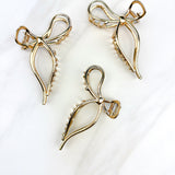 A group of gold metal One in a Million hair clips with a bow design, embodying elegance and style. Lilac Clip, 4.2 inches long, metal material, perfect for all hair types.