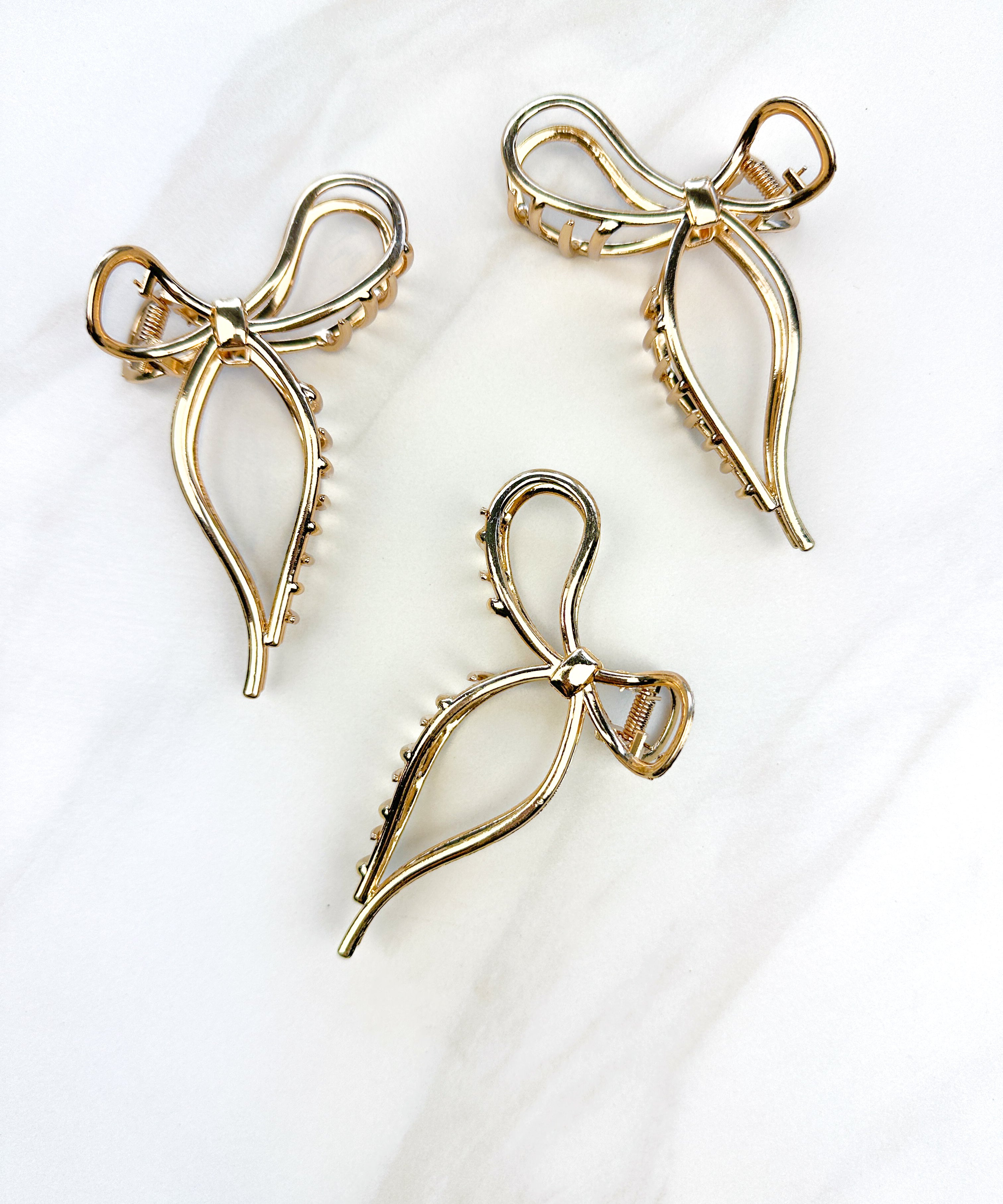 A group of gold metal One in a Million hair clips with a bow design, embodying elegance and style. Lilac Clip, 4.2 inches long, metal material, perfect for all hair types.