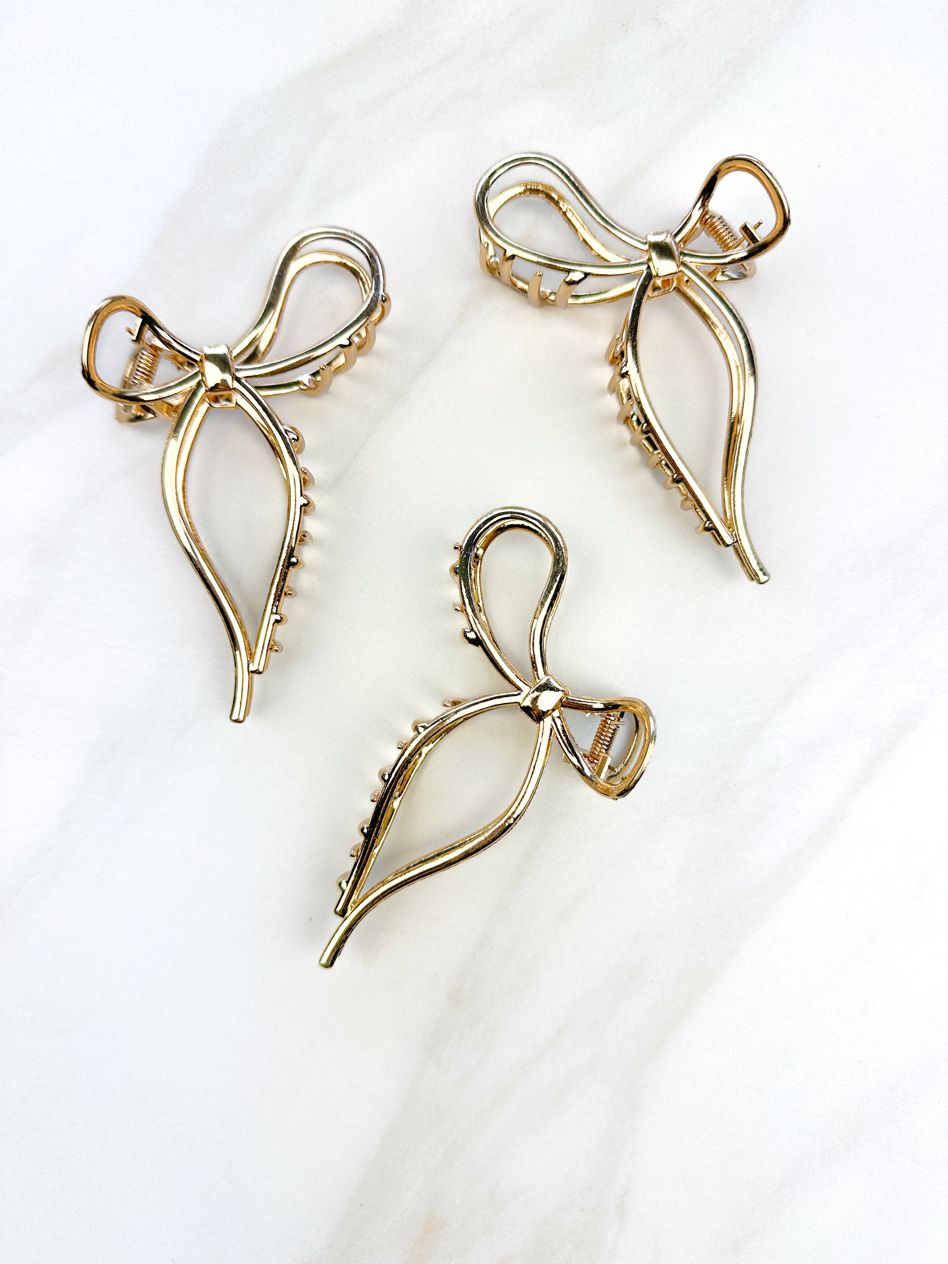 A group of gold metal One in a Million hair clips with a bow design, embodying elegance and style. Lilac Clip, 4.2 inches long, metal material, perfect for all hair types.