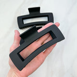 A close-up of a hand holding the black XL Essential Lilac Clip, a 4.8-inch matte hair accessory with a hinge closure. Perfect for all hair types.