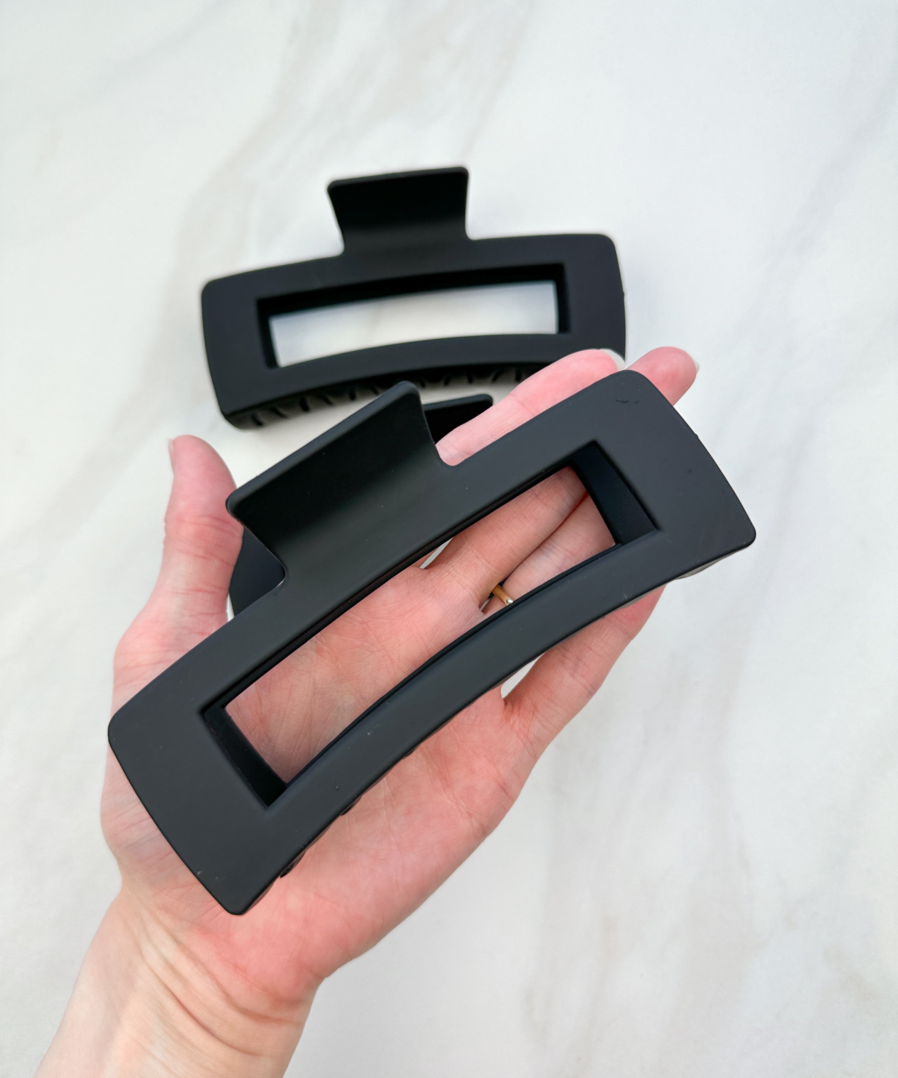 A close-up of a hand holding the black XL Essential Lilac Clip, a 4.8-inch matte hair accessory with a hinge closure. Perfect for all hair types.