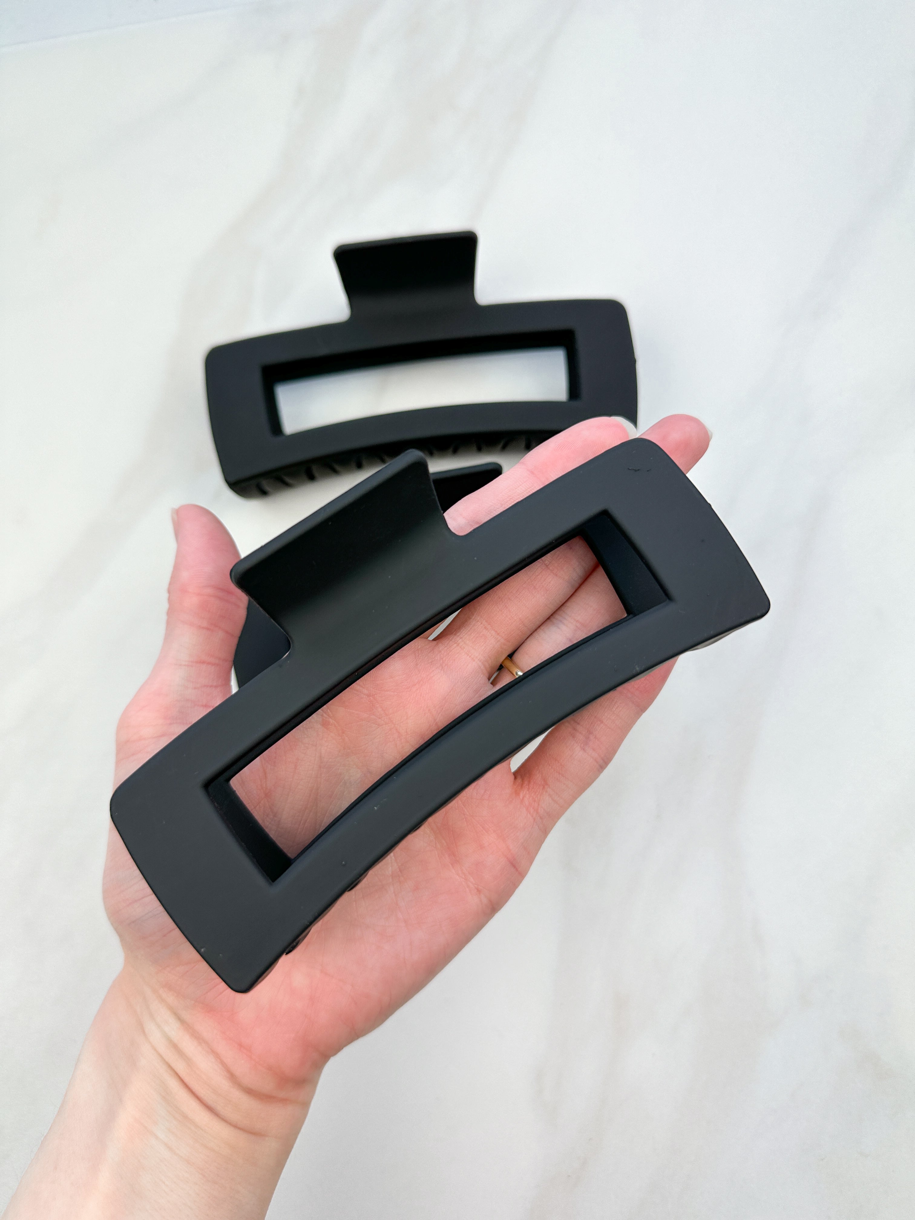 A close-up of a hand holding the black XL Essential Lilac Clip, a 4.8-inch matte hair accessory with a hinge closure. Perfect for all hair types.