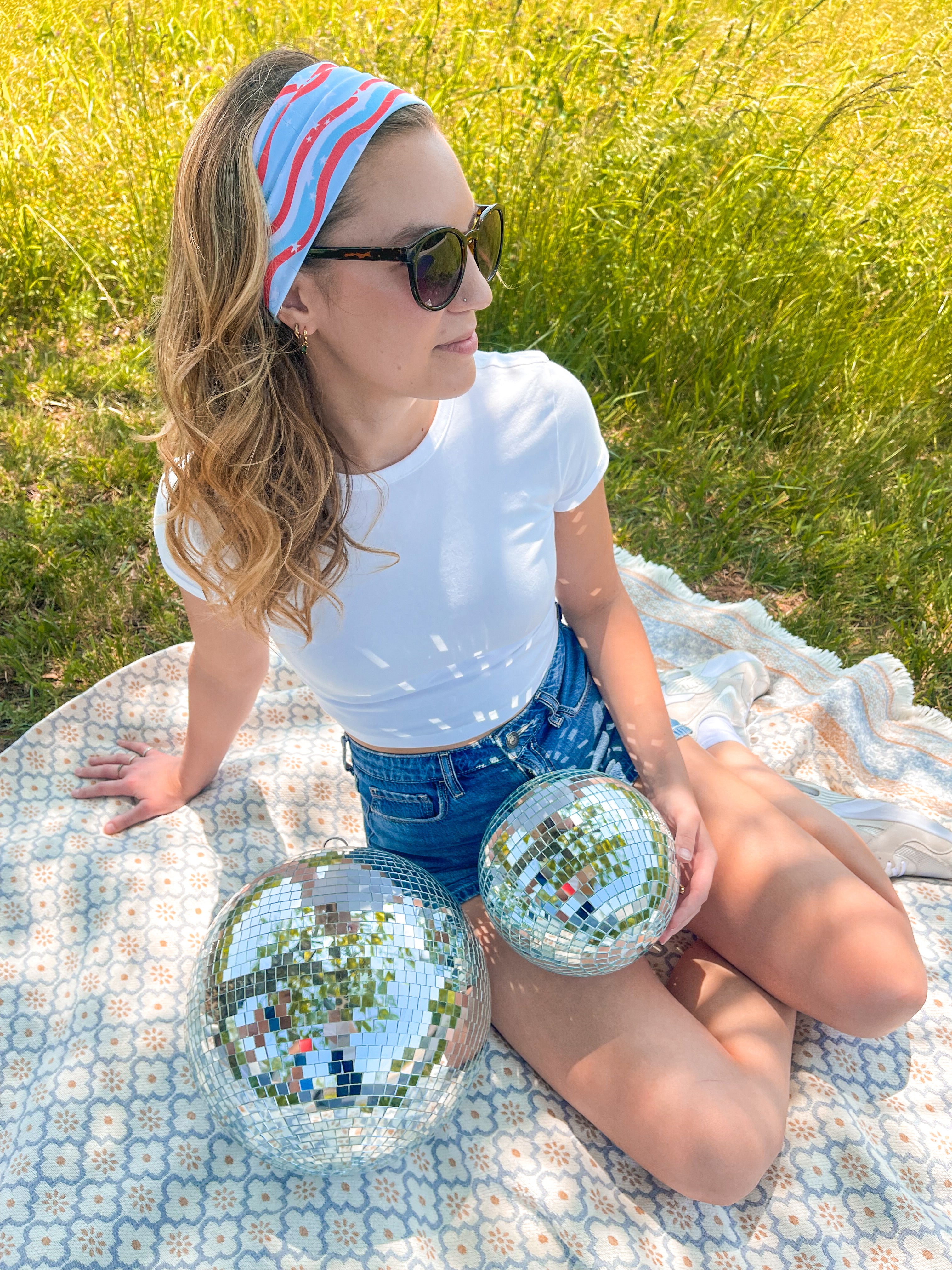 A woman confidently wears a Courtesy of Red, White and Blue headband outdoors, featuring a versatile 3-in-1 twist style for various looks. Designed for comfort and functionality, perfect for workouts or long shifts.