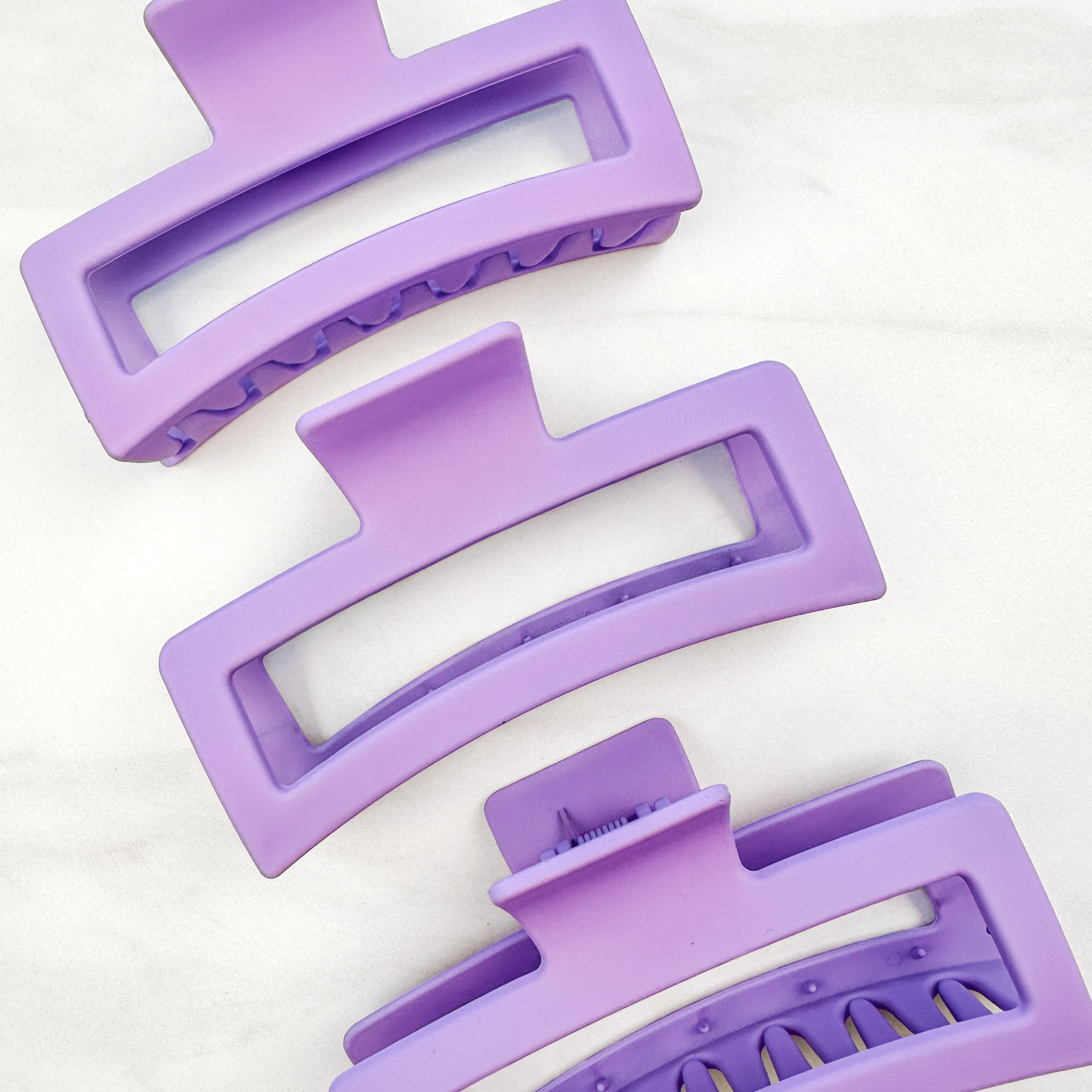 A group of purple Vacation Vibes Lilac Clips, 4.8 inches long, matte material, with a hinge closure. Perfect for all hair types, keeping hair out of your face.