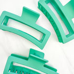 A group of green Vacation Vibes Lilac Clips, 4.8 inches long, matte material, with a hinge closure. Perfect for all hair types, keeping hair out of your face.