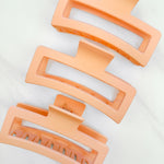 A group of orange Vacation Vibes Lilac Clips, 4.8 inches long, matte material, with a hinge closure. Perfect for all hair types, keeping hair out of your face.