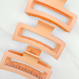 A group of orange Vacation Vibes Lilac Clips, 4.8 inches long, matte material, with a hinge closure. Perfect for all hair types, keeping hair out of your face.