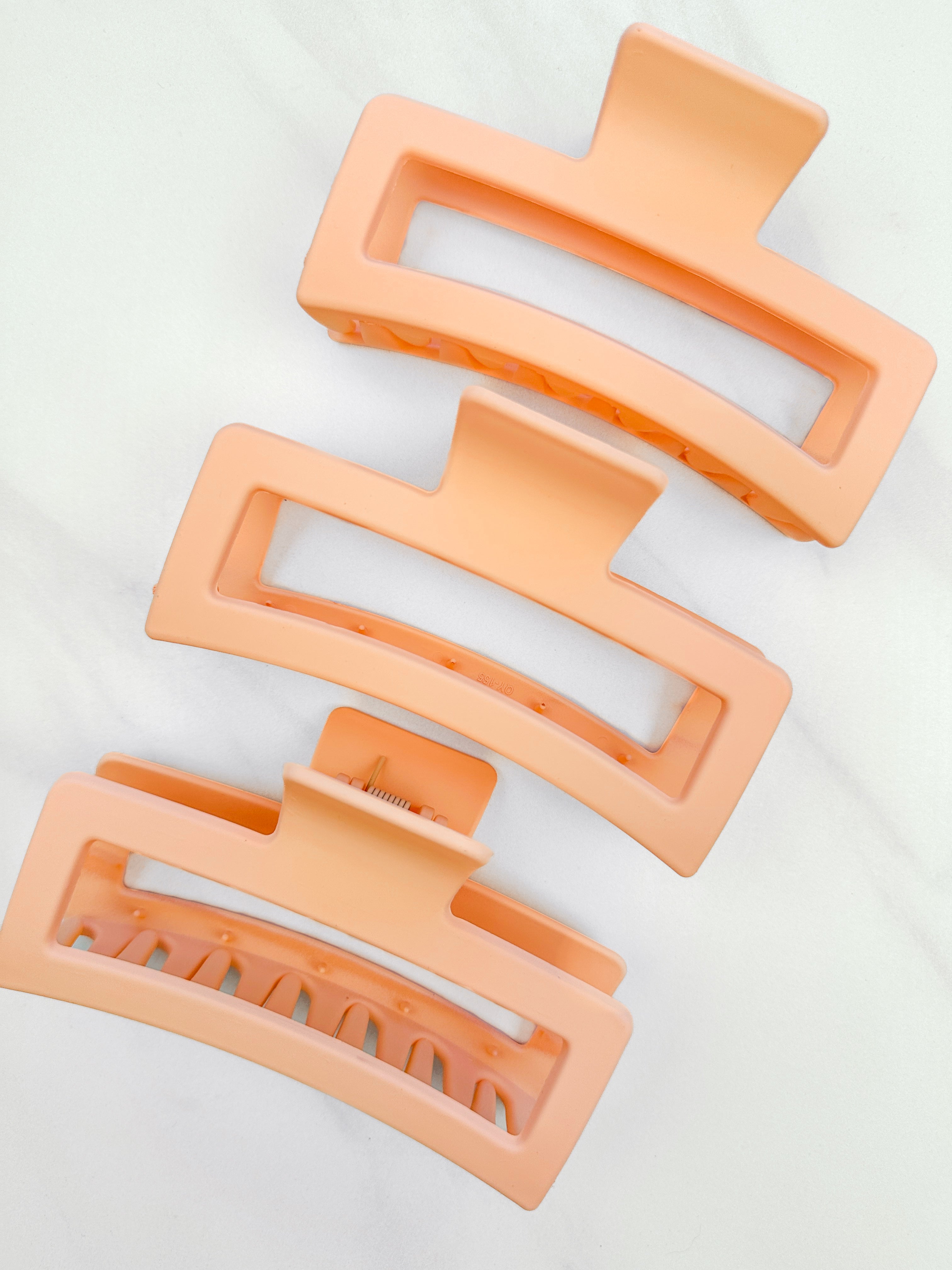 A group of orange Vacation Vibes Lilac Clips, 4.8 inches long, matte material, with a hinge closure. Perfect for all hair types, keeping hair out of your face.
