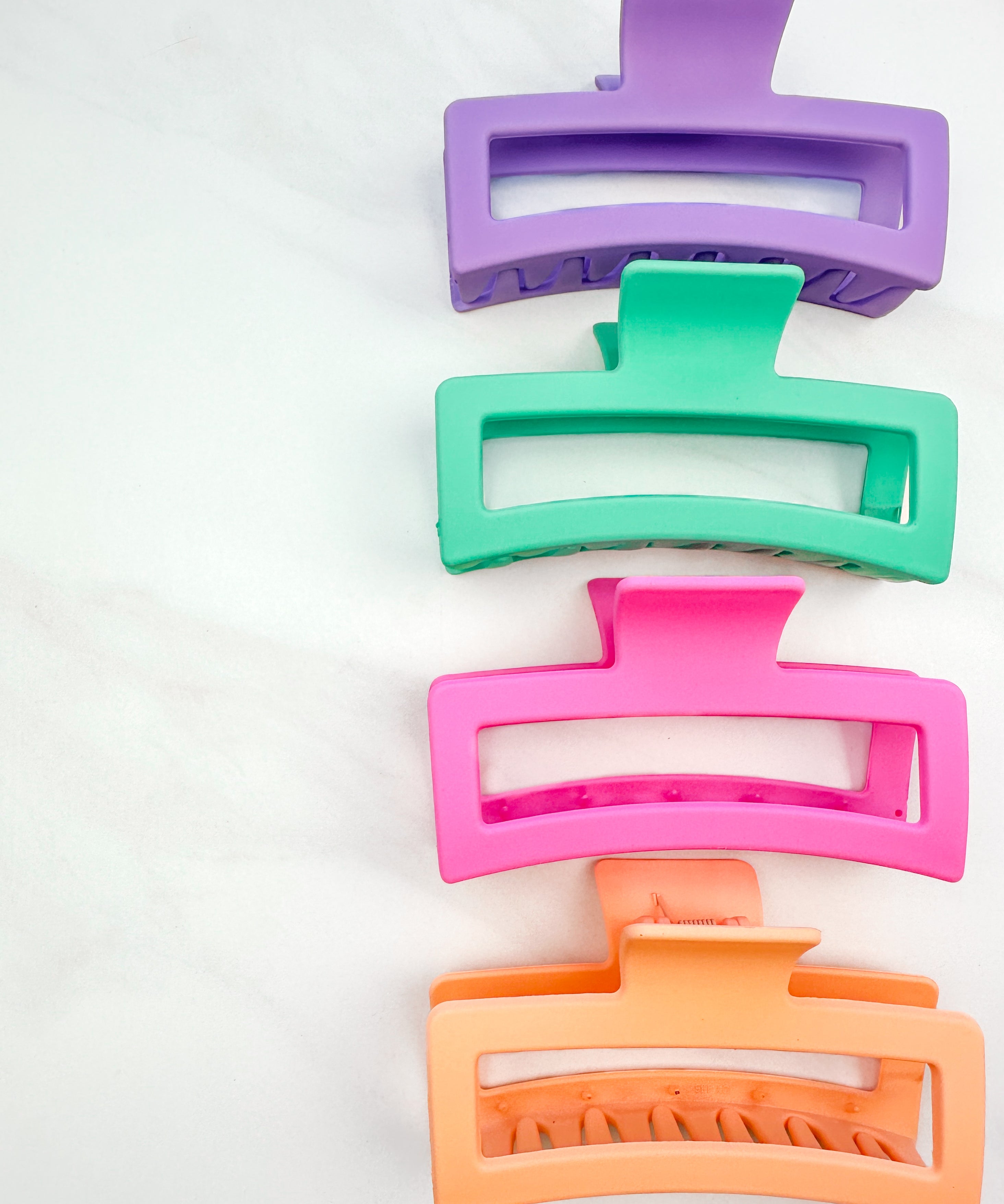 A group of various colors of Vacation Vibes Lilac Clips, 4.8 inches long, matte material, with a hinge closure. Perfect for all hair types, keeping hair out of your face.