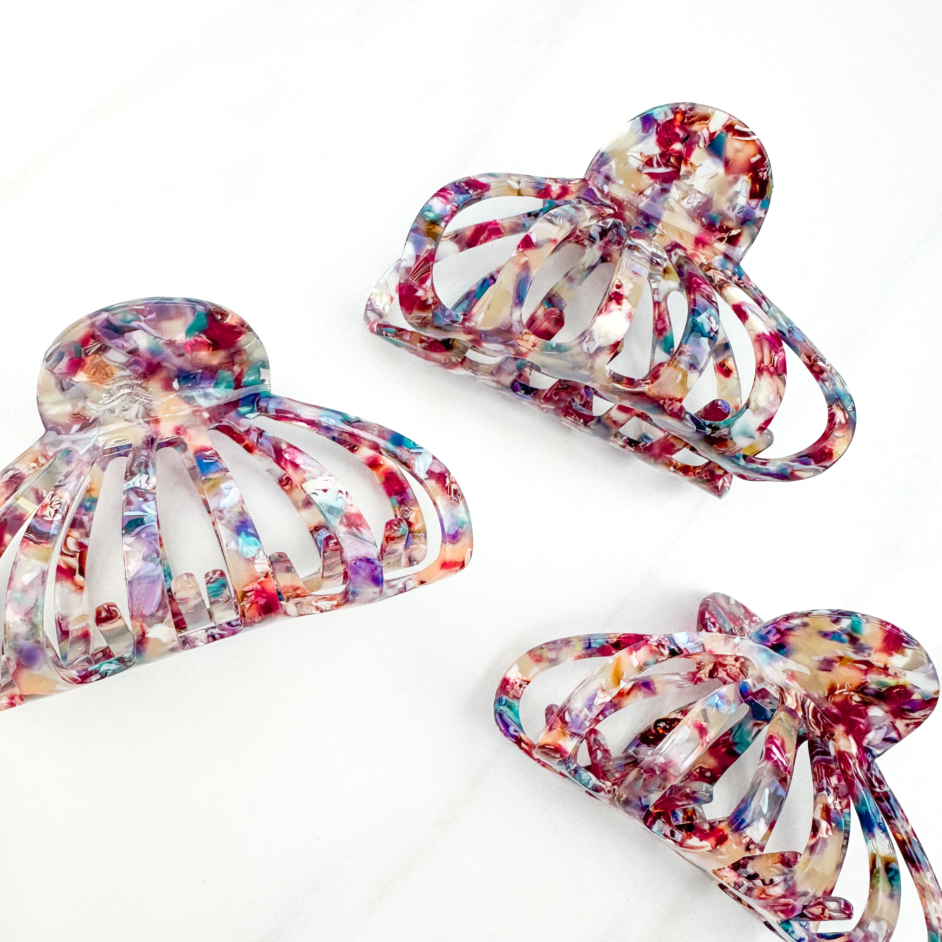 A group of Karma Lilac Clips, a fashionable hair accessory with a glossy rainbow material and a hinge closure. Perfect for all hair types and textures.