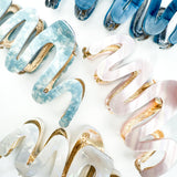 A group of zig zag-shaped marble hair clips with gold trim, including pink, blue, white and dark blue clips.