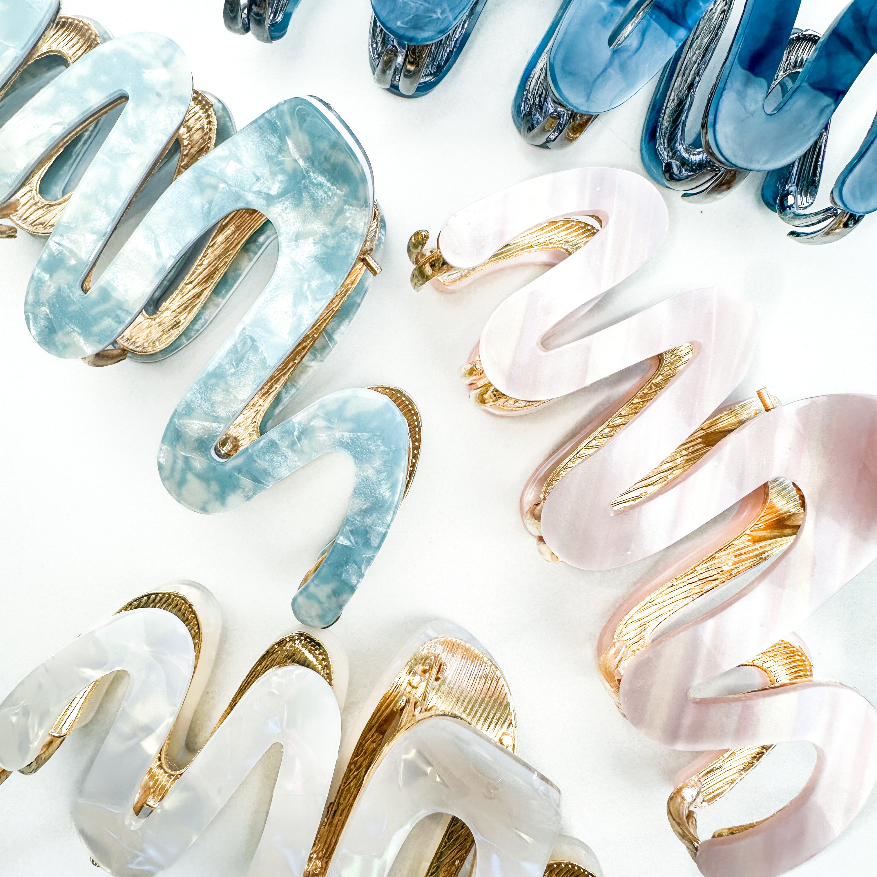 A group of zig zag-shaped marble hair clips with gold trim, including pink, blue, white and dark blue clips.