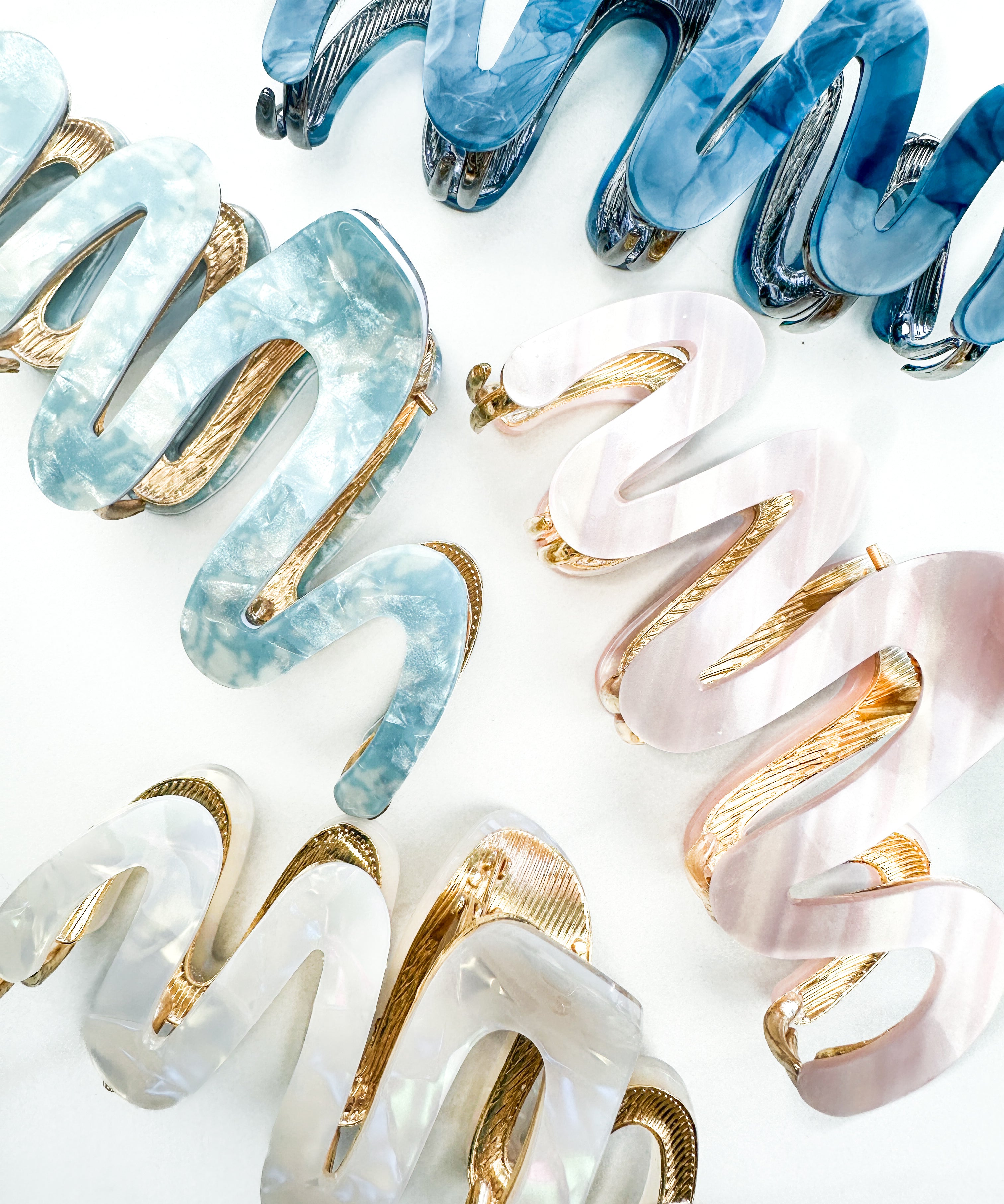A group of zig zag-shaped marble hair clips with gold trim, including pink, blue, white and dark blue clips.