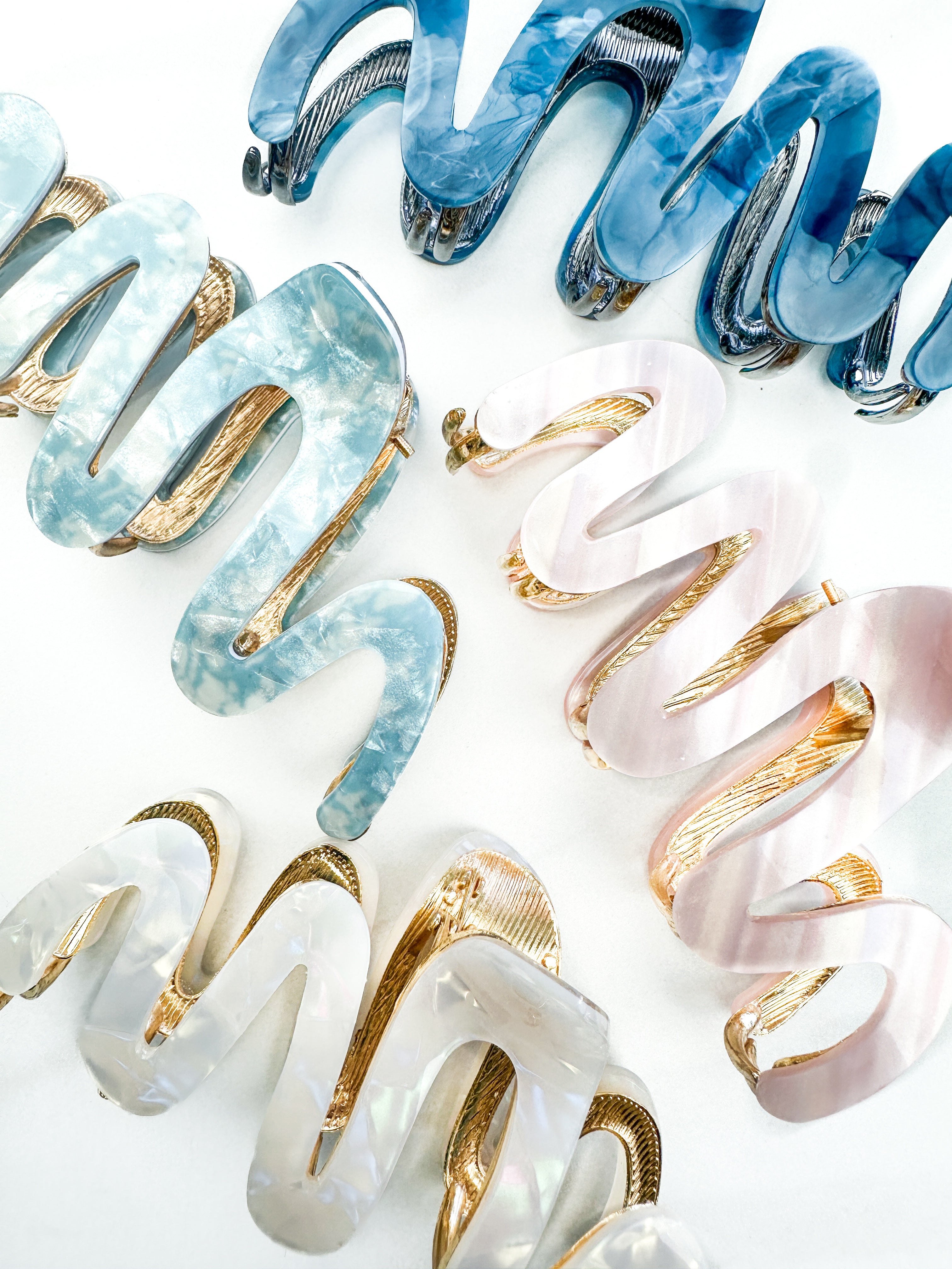 A group of zig zag-shaped marble hair clips with gold trim, including pink, blue, white and dark blue clips.