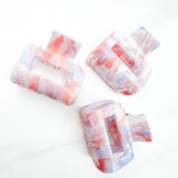 A group of plastic hair clips, including the Head in the Clouds Lilac Clip, on a white surface.