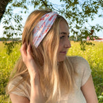 Woman smiling while wearing You Herd Me headband in a field, showcasing its versatile 3-in-1 twist style and buttery-soft, ultra-stretchy poly-knit blend.