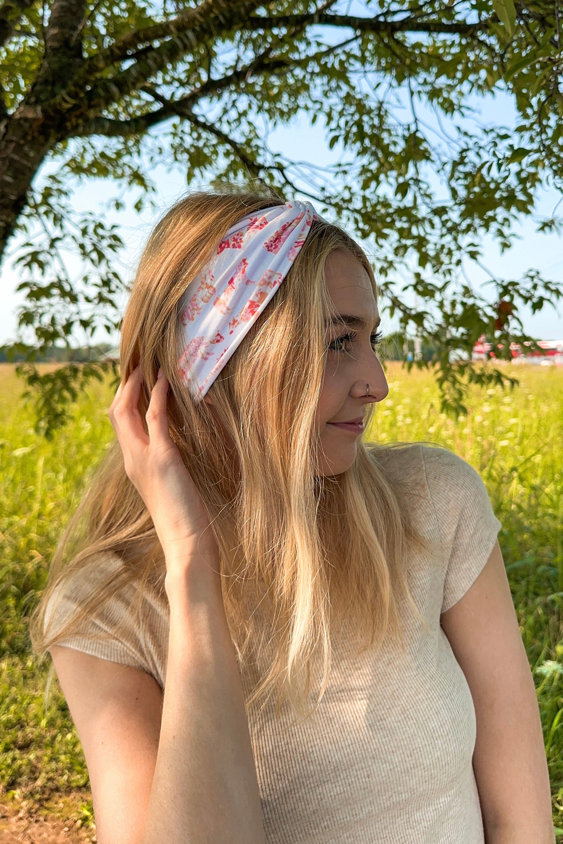 Woman smiling while wearing You Herd Me headband in a field, showcasing its versatile 3-in-1 twist style and buttery-soft, ultra-stretchy poly-knit blend.
