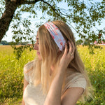 Woman smiling while wearing You Herd Me headband in a field, showcasing its versatile 3-in-1 twist style and buttery-soft, ultra-stretchy poly-knit blend.
