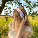 Woman smiling while wearing You Herd Me headband in a field, showcasing its versatile 3-in-1 twist style and buttery-soft, ultra-stretchy poly-knit blend.