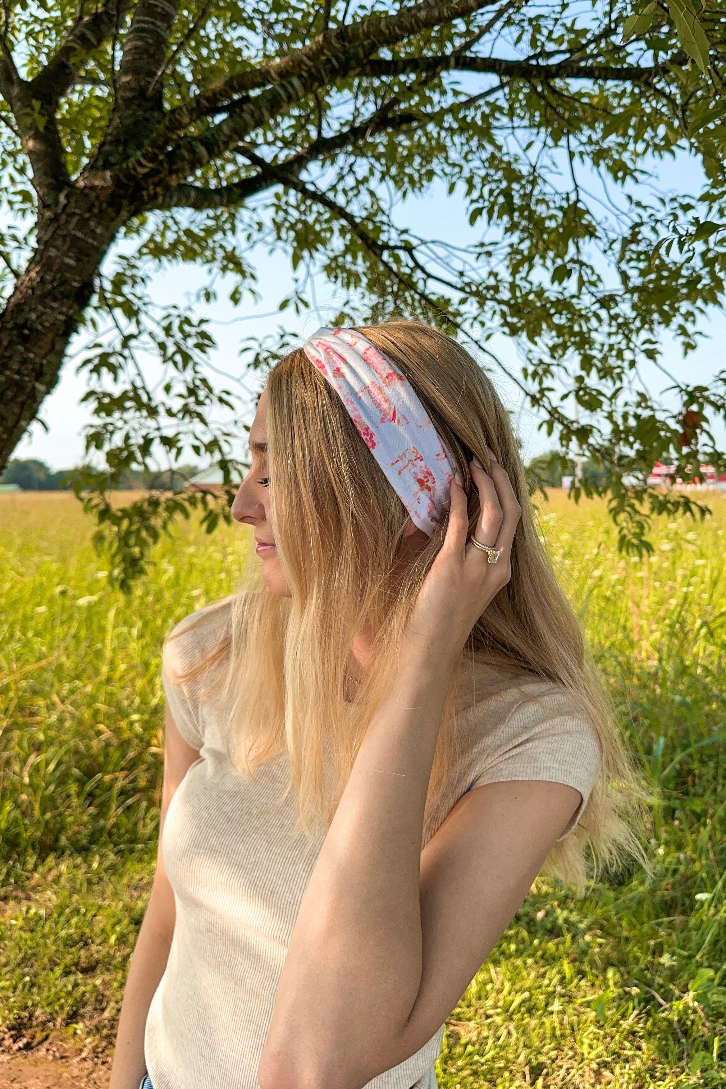 Woman smiling while wearing You Herd Me headband in a field, showcasing its versatile 3-in-1 twist style and buttery-soft, ultra-stretchy poly-knit blend.