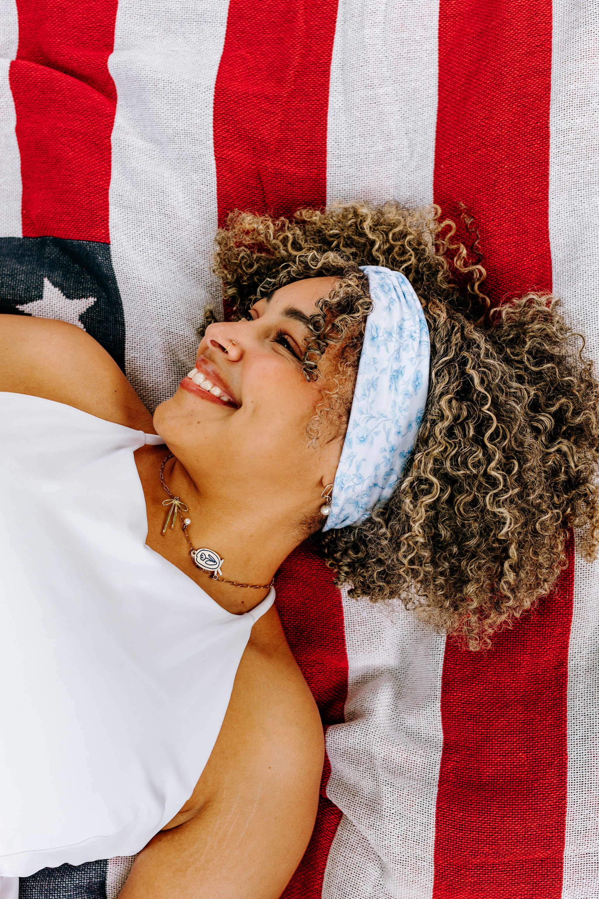 Woman with curly hair type happily wearing the most comfortable hand-made headband in the print Daisy Floral on Ivory. 