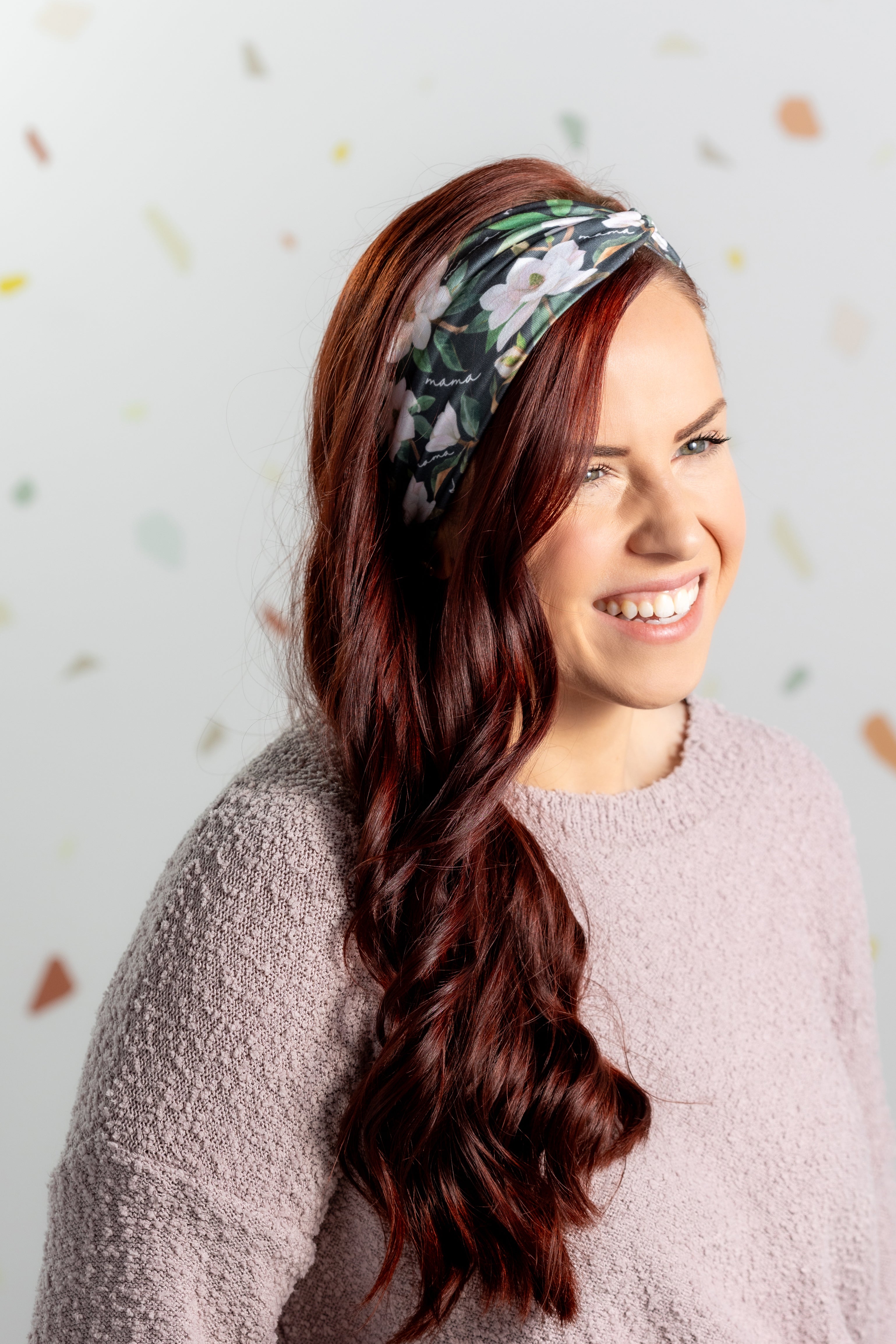A black headband with white floral pattern and "Mama" script, offering confidence and functionality. Features one size fits most, machine washable, ultra stretchy poly-knit blend, versatile 3-in-1 twist style, sweat absorbent double-layer fabric.