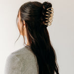 A woman wearing a gold Out Of Office Lilac clip, showcasing the half-up hairstyle. 3.6 inches long, shiny gold metal, perfect for all hair types. Hinge closure for a secure fit.