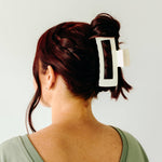 A woman wearing a white XL Essential Lilac Clip, a matte hair accessory with a hinge closure. 4.8 inches long, suitable for all hair types.