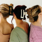 Three women wearing various XL Essential Lilac Clips, a matte hair accessory with a hinge closure. 4.8 inches long, suitable for all hair types.