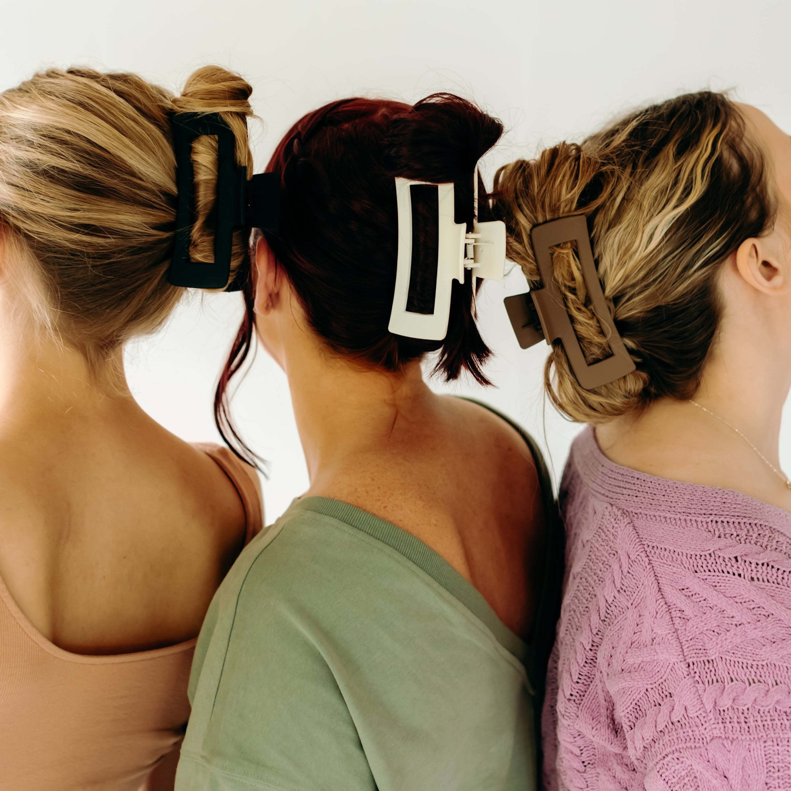 Three women wearing various XL Essential Lilac Clips, a matte hair accessory with a hinge closure. 4.8 inches long, suitable for all hair types.