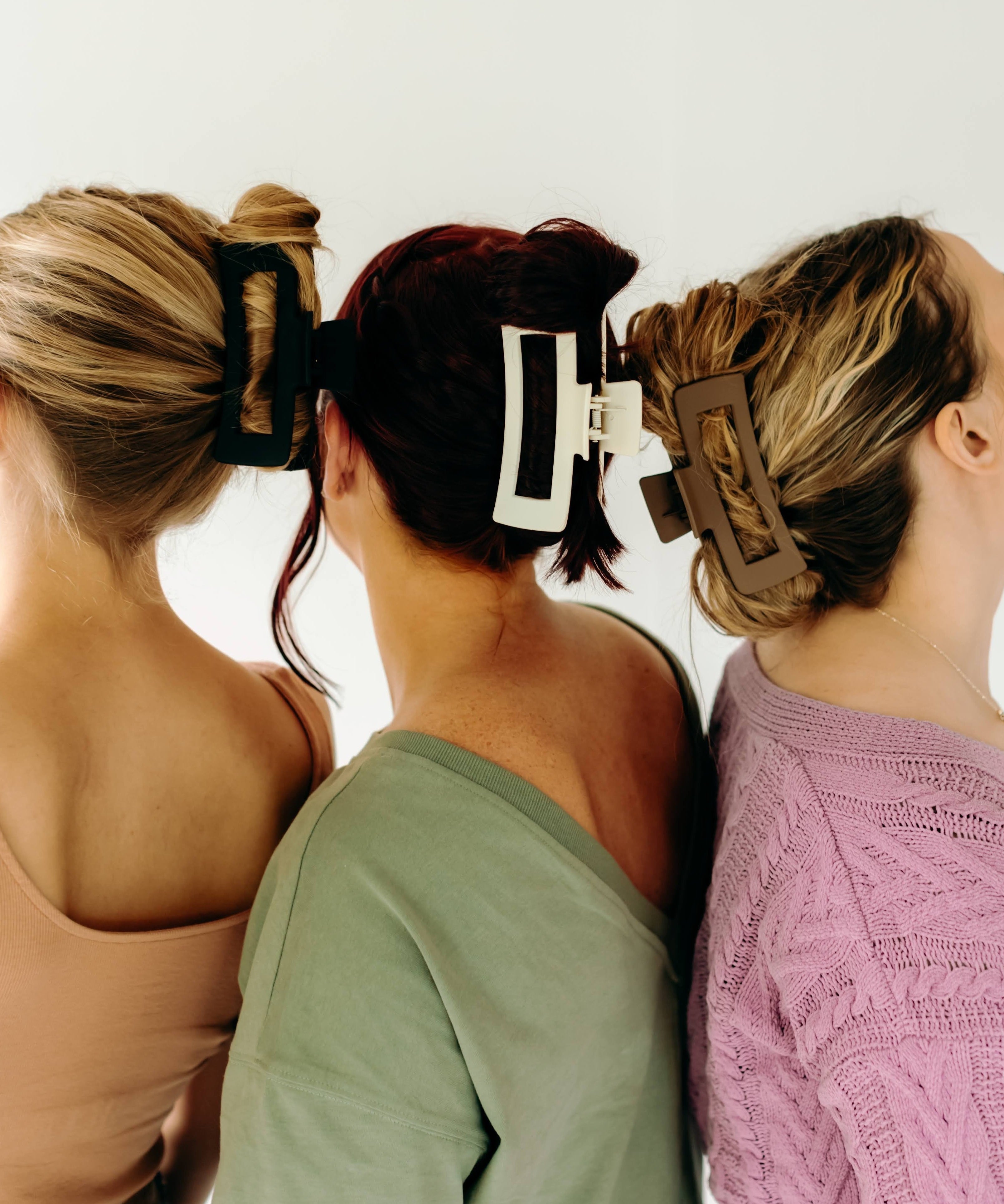 Three women wearing various XL Essential Lilac Clips, a matte hair accessory with a hinge closure. 4.8 inches long, suitable for all hair types.