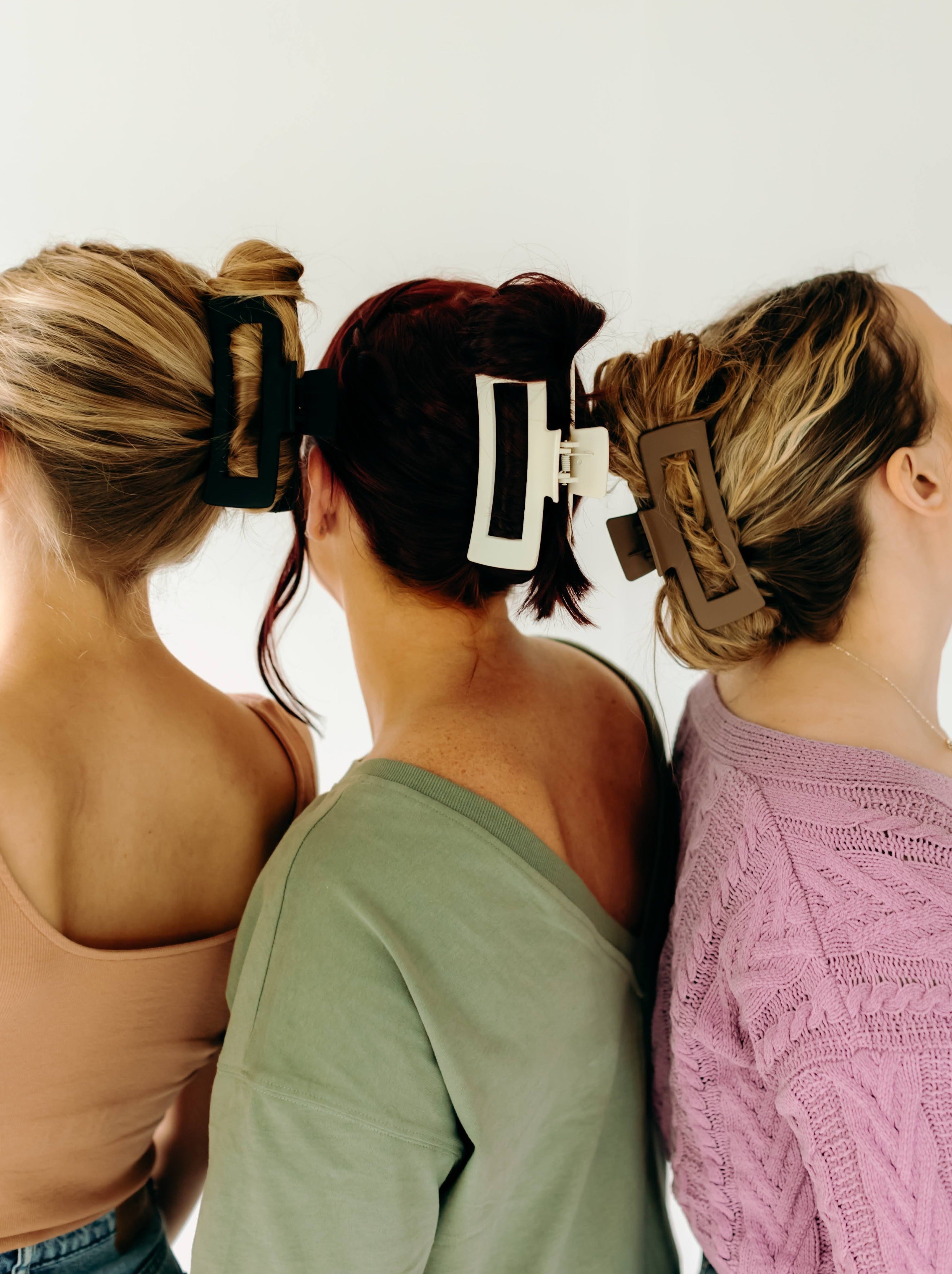 Three women wearing various XL Essential Lilac Clips, a matte hair accessory with a hinge closure. 4.8 inches long, suitable for all hair types.