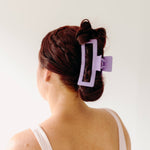 A woman wearing a purple Vacation Vibes Lilac Clip in her hair, a fashion accessory perfect for all hair types. Matte material, 4.8 inches long, with a hinge closure.