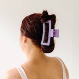 A woman wearing a purple Vacation Vibes Lilac Clip in her hair, a fashion accessory perfect for all hair types. Matte material, 4.8 inches long, with a hinge closure.