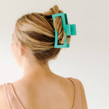 A woman wearing a green Vacation Vibes Lilac Clip in her hair, a fashion accessory perfect for all hair types. Matte material, 4.8 inches long, with a hinge closure.