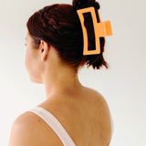 A woman wearing an orange Vacation Vibes Lilac Clip in her hair, a fashion accessory perfect for all hair types. Matte material, 4.8 inches long, with a hinge closure.