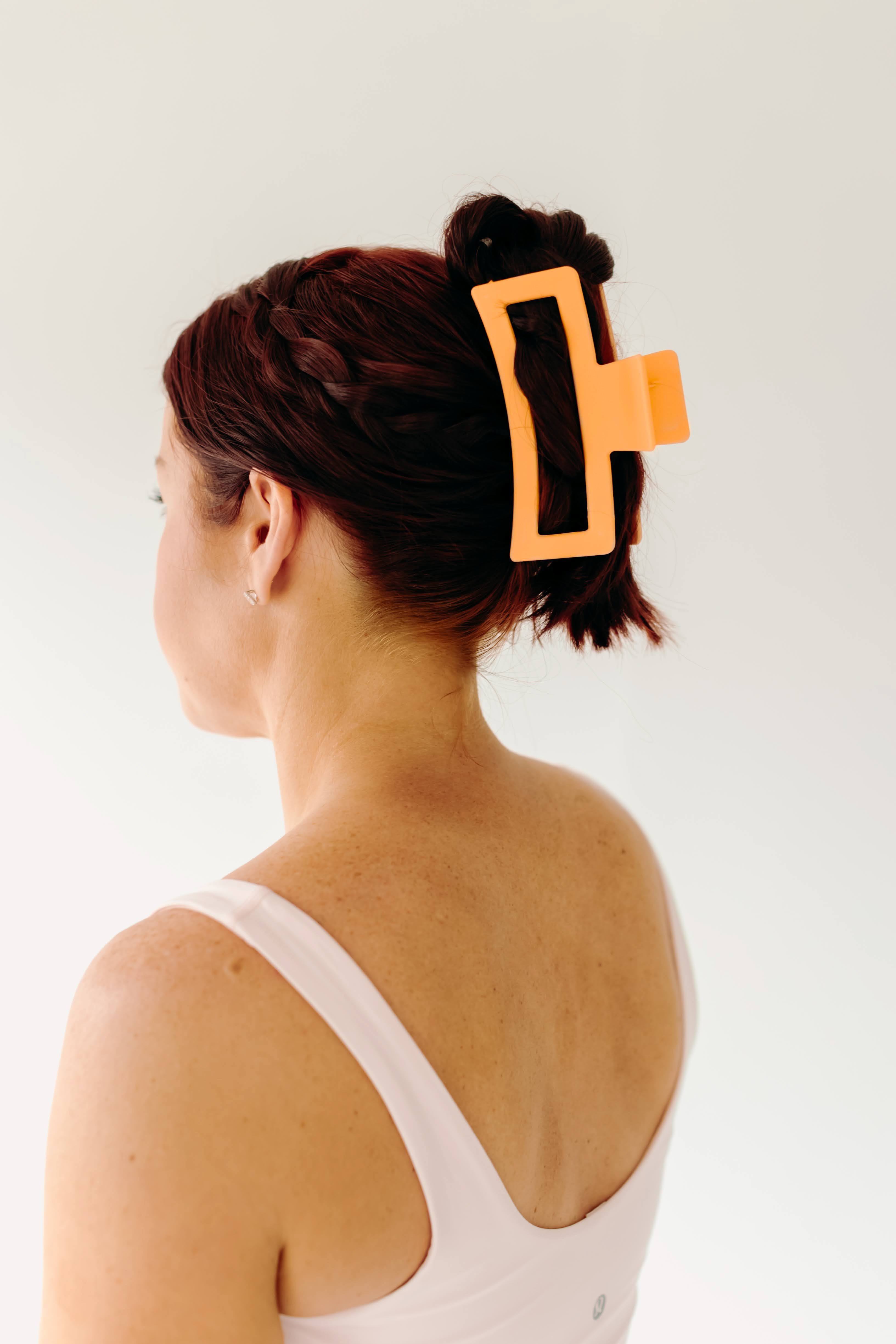 A woman wearing an orange Vacation Vibes Lilac Clip in her hair, a fashion accessory perfect for all hair types. Matte material, 4.8 inches long, with a hinge closure.