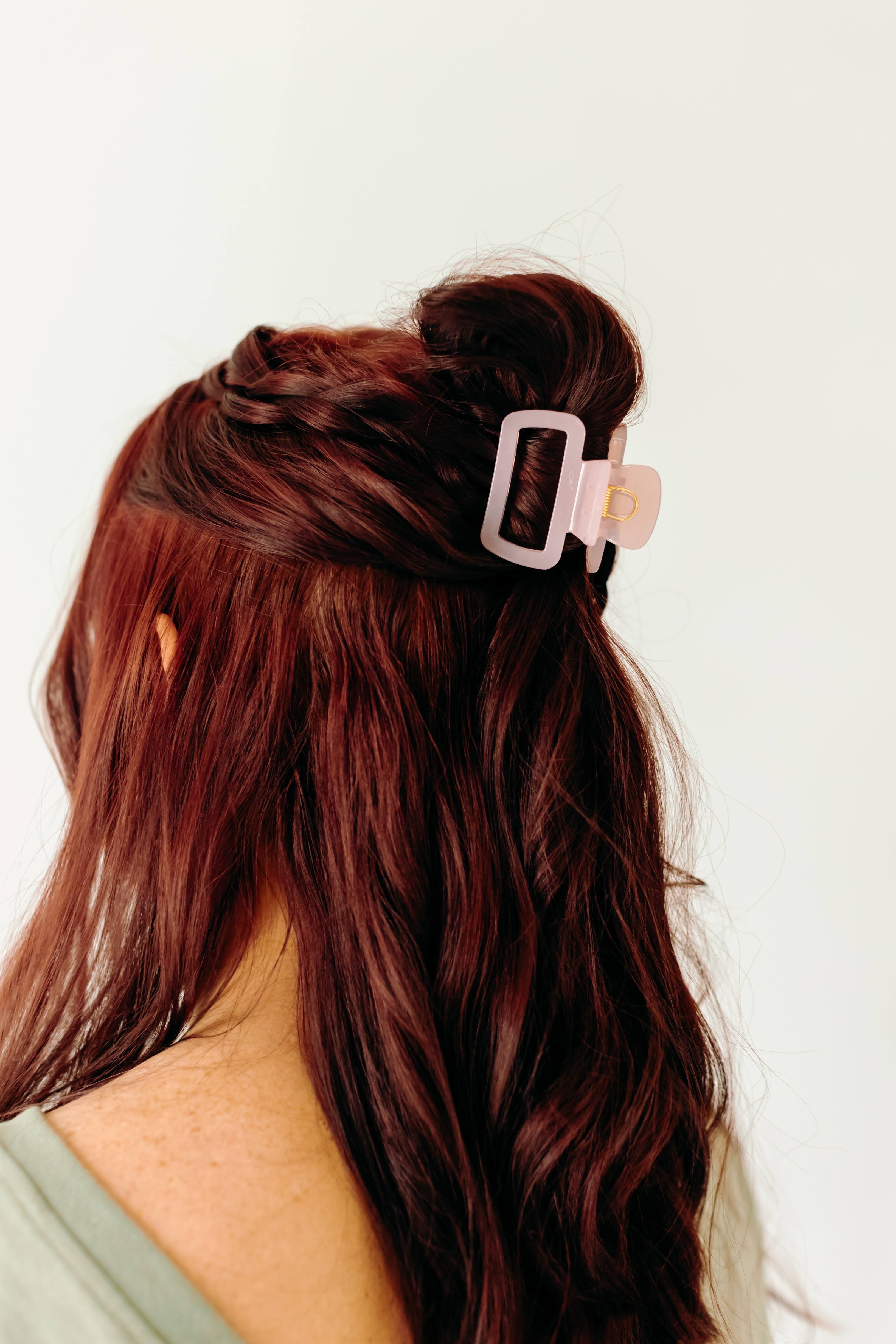 A woman wearing a pink Happy Hour Lilac Clip, a glossy hair accessory with a hinge closure. Perfect for all hair types. Size: 1.8 inches long.