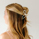 A woman with stylish hair wearing a One in a Million white hair clip, showcasing the Lilac Clip, a 4.2-inch metal claw clip with a hinge closure for all hair types.