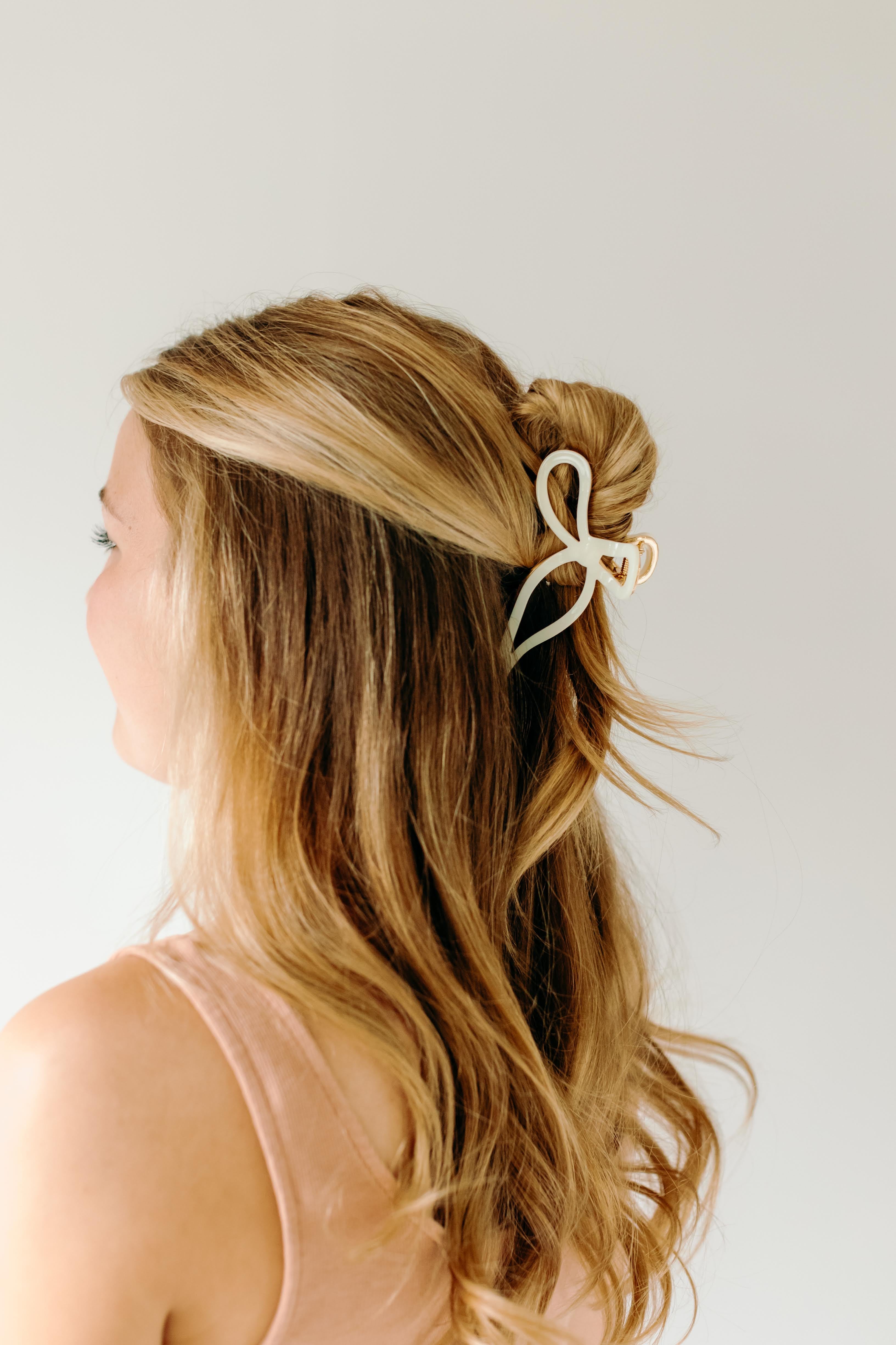 A woman with stylish hair wearing a One in a Million white hair clip, showcasing the Lilac Clip, a 4.2-inch metal claw clip with a hinge closure for all hair types.