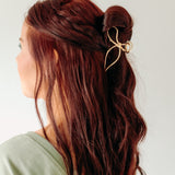 A woman with stylish hair wearing a One in a Million gold hair clip, showcasing the Lilac Clip, a 4.2-inch metal claw clip with a hinge closure for all hair types.