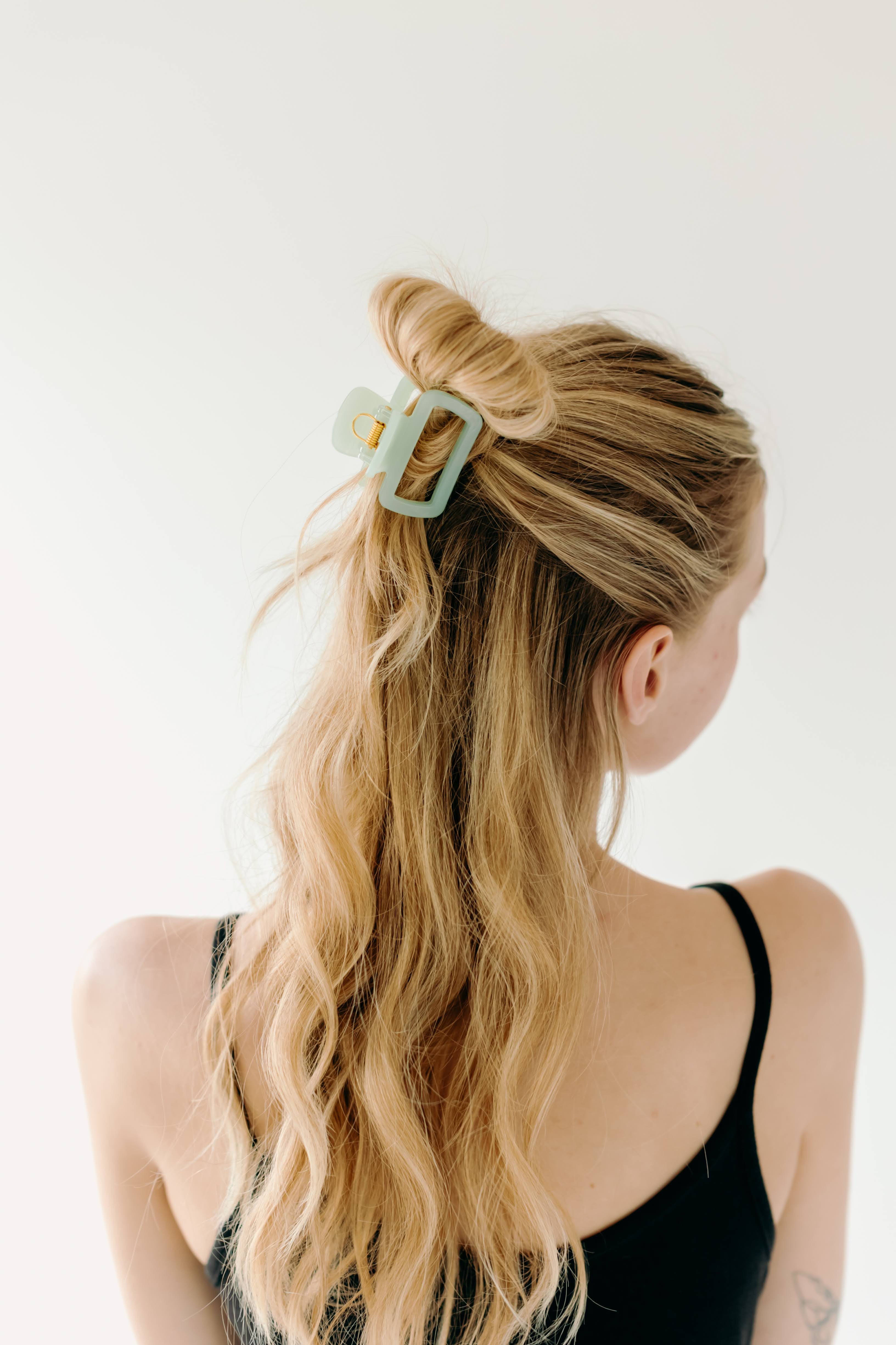 A woman wearing a green Happy Hour Lilac Clip, a glossy hair accessory with a hinge closure. Perfect for all hair types. Size: 1.8 inches long.