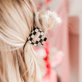 Checking In Lilac Clip: a 2-inch glossy checkered claw clip with a hinge closure, perfect for styling and keeping hair in place.