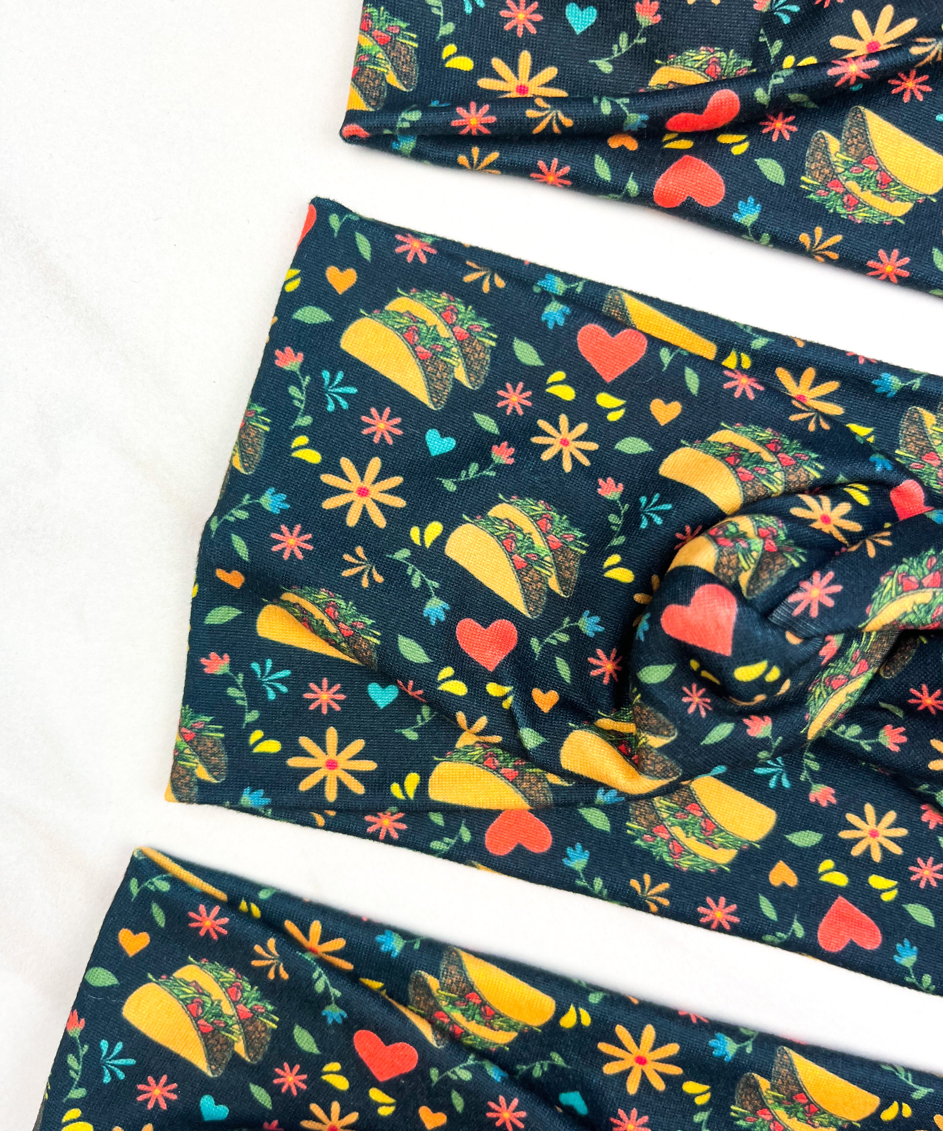 Adult women's black headband with a pair of tacos, red hearts, and small red and yellow flowers and green leaf print