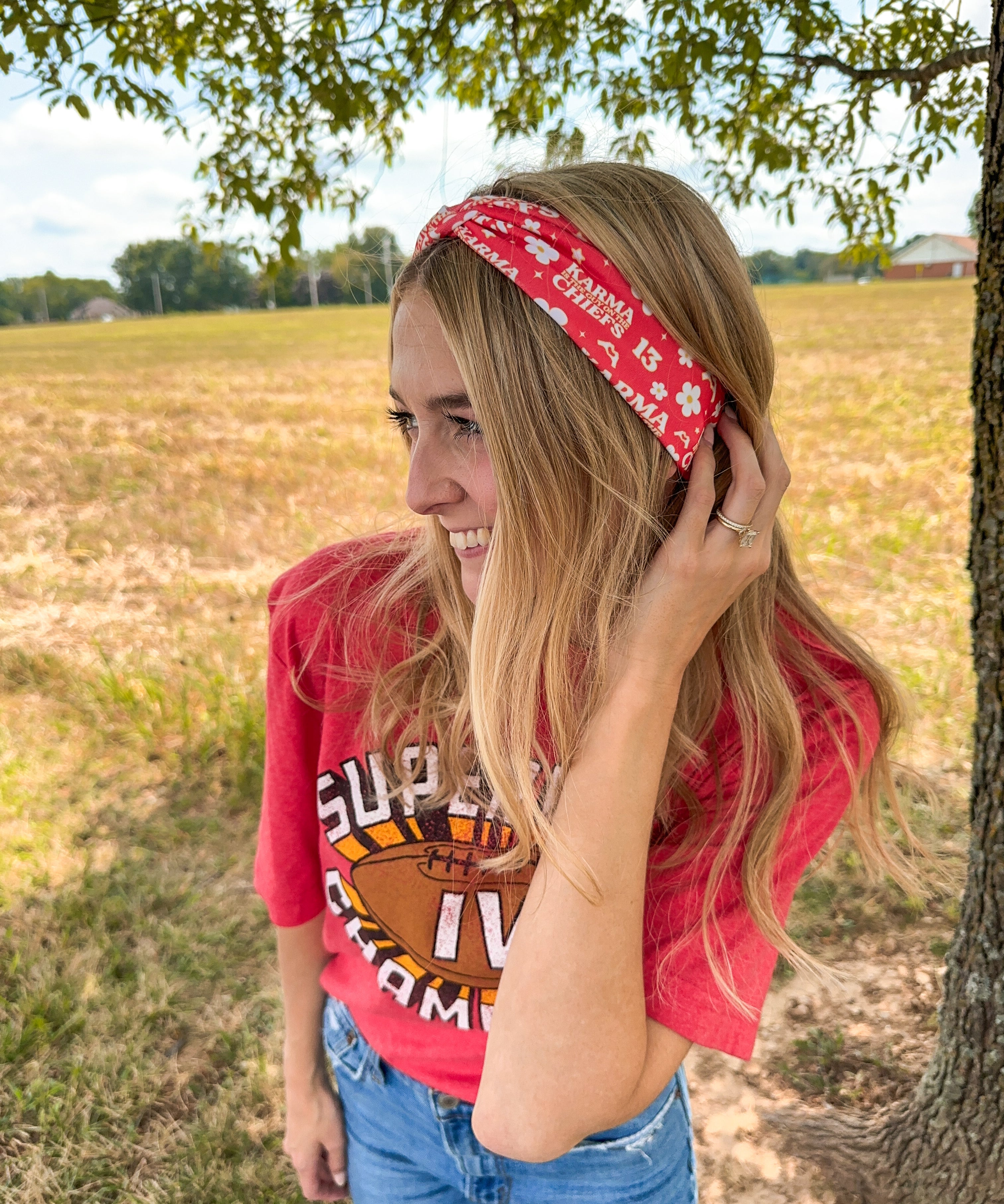 Woman smiling in a red Karma Is the Guy on the Chiefs headband, showcasing its versatile, functional design for workouts, long shifts, or playdays.