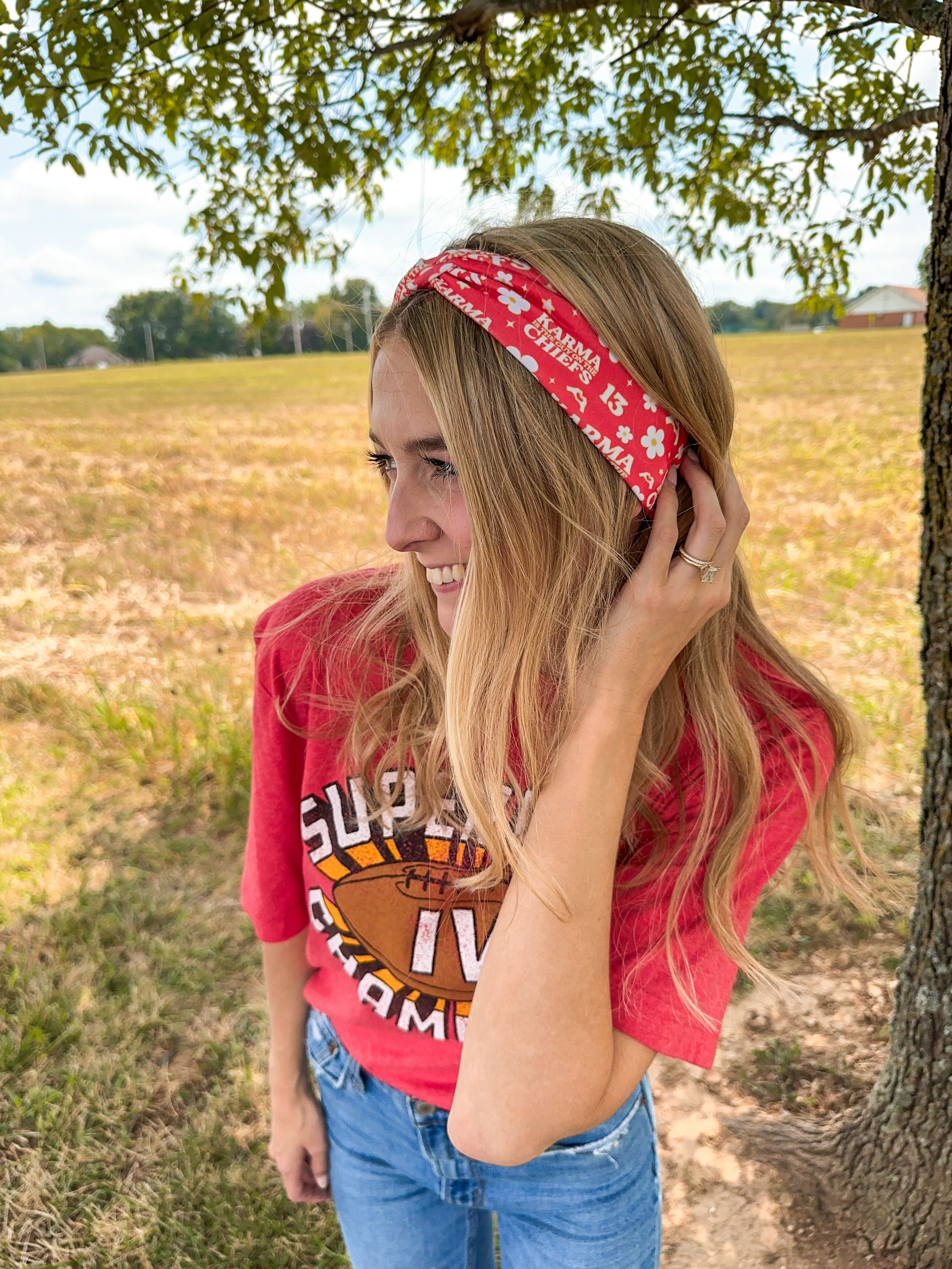 Woman smiling in a red Karma Is the Guy on the Chiefs headband, showcasing its versatile, functional design for workouts, long shifts, or playdays.